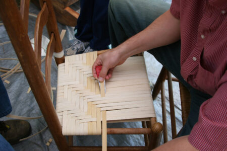 closeup of hands demonstrating how to use a cane weaving tool